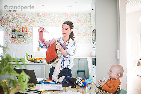 Berufstätige Mutter hält Stoffmuster in der Hand  während das Mädchen in der Küche im Heimbüro wegschaut
