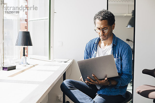 Computerprogrammierer  der am Laptop arbeitet  während er im Büro am Fenster sitzt