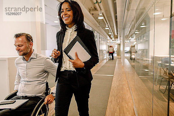Lächelnde Geschäftsfrau mit behindertem männlichen Manager im Bürokorridor