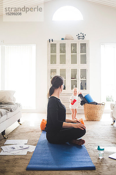 Berufstätige Mutter übt Yoga in voller Länge aus  während die Tochter im Wohnzimmer spielt