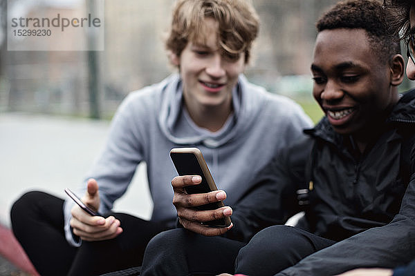 Telefon süchtig machende glückliche Freunde sitzen auf dem Bürgersteig in der Stadt