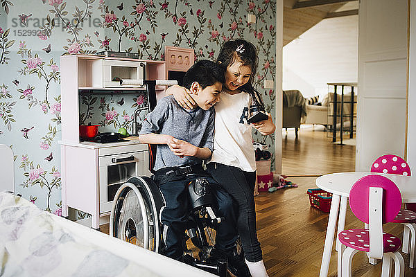 Fröhliche Schwester schaut sich zu Hause mit ihrem autistischen Bruder auf dem Handy ein Video an