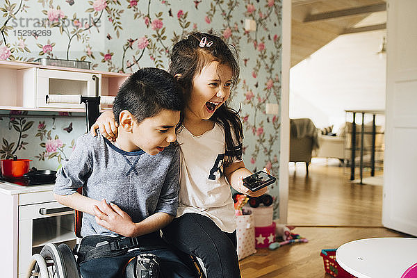 Fröhliche Schwester schaut sich zu Hause mit ihrem autistischen Bruder auf einem Smartphone ein Video an