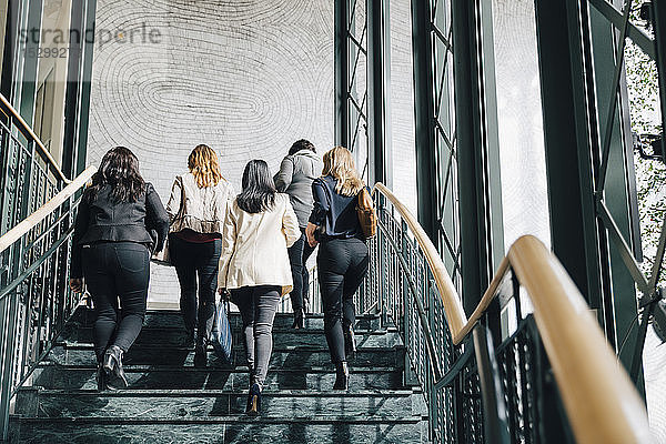 Niedriger Blickwinkel auf multiethnische Unternehmerinnen  die sich im Büro auf einer Treppe nach oben bewegen