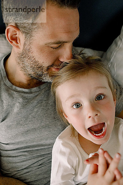 Porträt eines schreienden Mädchens im Bett liegend mit Vater im Schlafzimmer