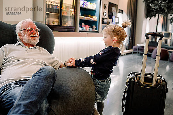 Seitenansicht eines Mädchens  das den Großvater zieht  der auf einem Sessel in der Hotellobby sitzt