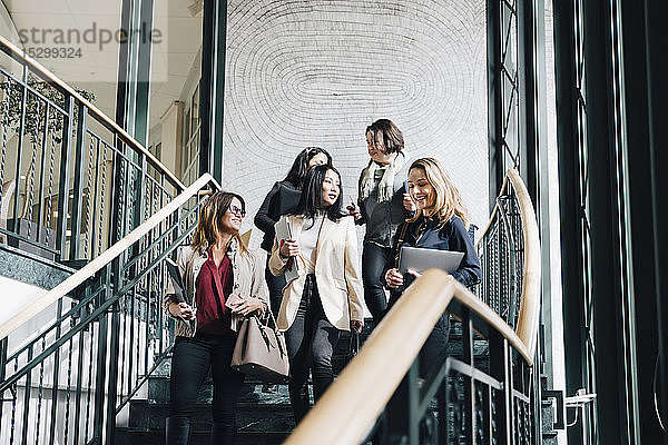 Niedriger Blickwinkel auf lächelnde Unternehmerinnen  die sich im Büro auf der Treppe nach unten bewegen