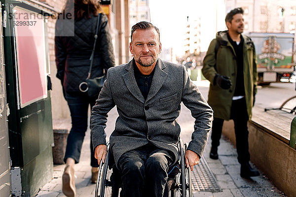 Behinderter reifer Mann schaut weg  während er in der Stadt im Rollstuhl sitzt
