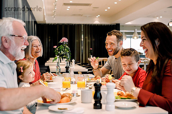 Fröhliche Familie unterhält sich beim Essen am Tisch im Restaurant