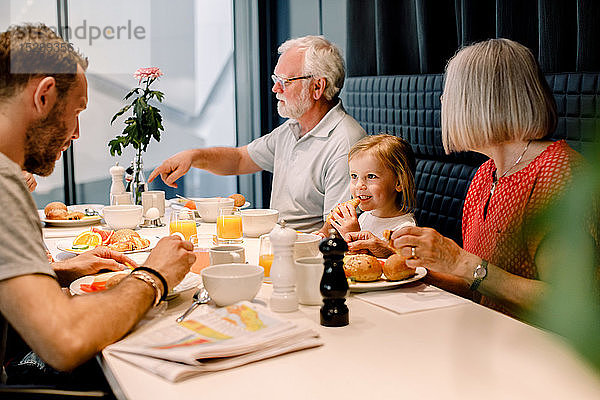 Lächelndes Mädchen schaut den Vater an  während es mit den Großeltern im Restaurant isst