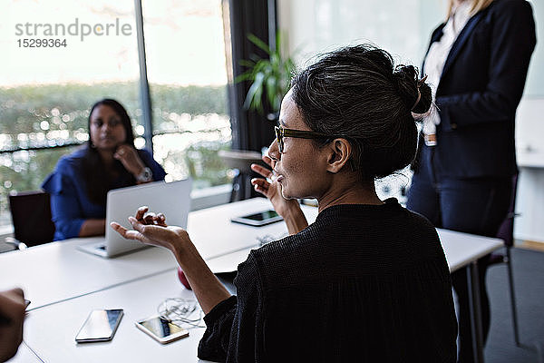 Geschäftsfrau gestikuliert während einer Diskussion mit Kollegen während einer Sitzung am Konferenztisch im Sitzungssaal