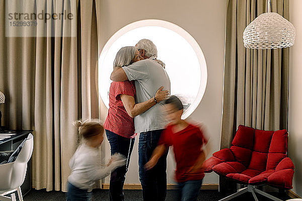 Älteres Ehepaar umarmt sich  während die Enkel im Zimmer spielen