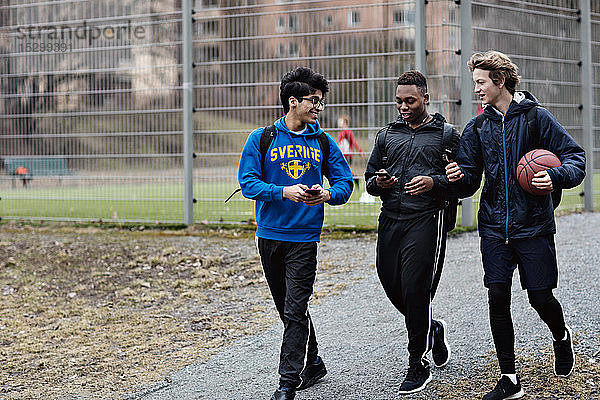 Glückliche Freunde benutzen Mobiltelefone  während sie auf der Straße gegen ein Sportgericht laufen