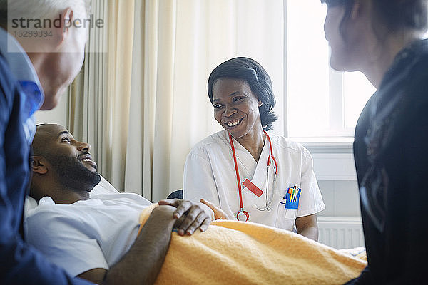 Lächelnde Ärztin im Gespräch mit Patient und Familie auf der Krankenhausstation