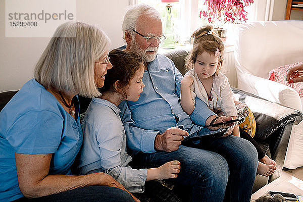 Großeltern und Enkelkinder benutzen digitales Tablet  während sie zu Hause im Wohnzimmer sitzen