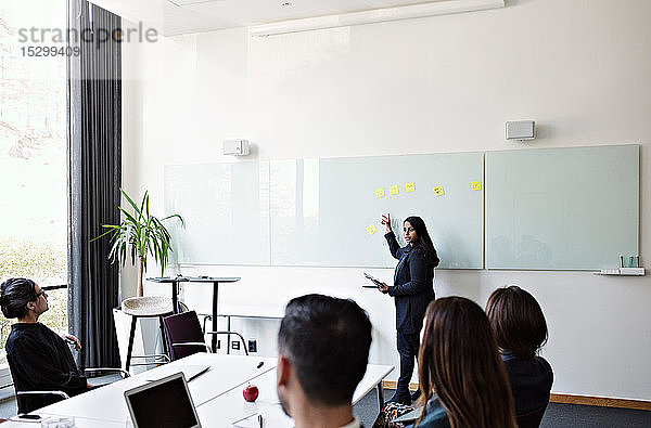 Geschäftsfrau gestikuliert über das Whiteboard  während sie bei einer Besprechung im Büro mit Kollegen diskutiert