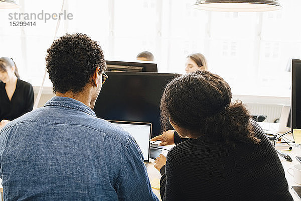 Rückansicht der Mitarbeiter  die die Codierung über Laptop auf dem Schreibtisch im Büro diskutieren