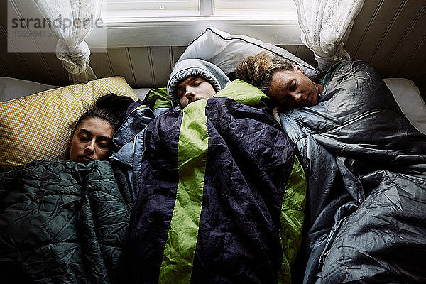 Schrägansicht von Freundinnen und Freunden  die zusammen auf einem Bett in einer Hütte schlafen