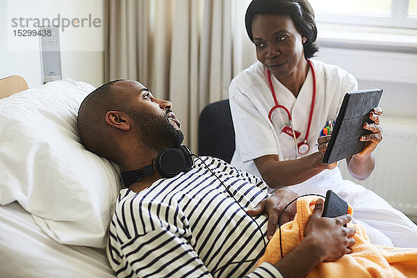 Ärztin zeigt junger Patientin digitales Tablett während eines Besuchs auf der Krankenhausstation