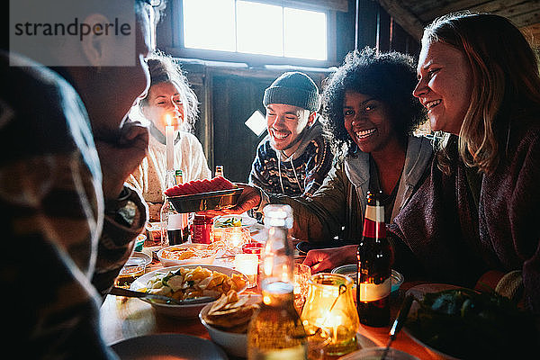 Männliche und weibliche Freunde unterhalten sich beim Essen auf dem Tisch im Blockhaus