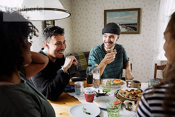 Fröhliche Freunde unterhalten sich beim Essen in geselliger Runde zu Hause