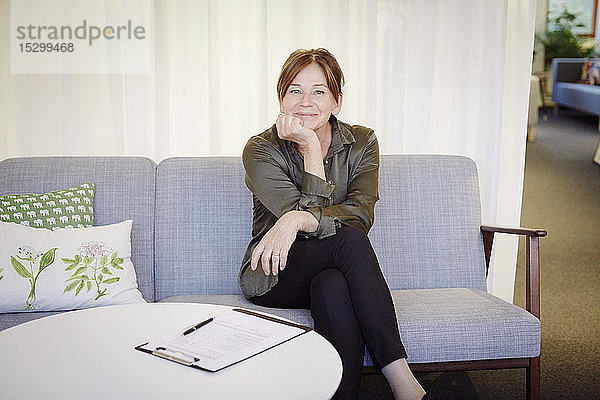 Porträt einer selbstbewusst lächelnden Psychologin  die bei einem Workshop auf dem Sofa sitzt