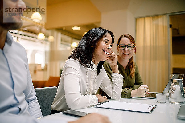 Fröhliche Geschäftsfrauen sitzen am Konferenztisch während einer Verkaufssitzung im Büro