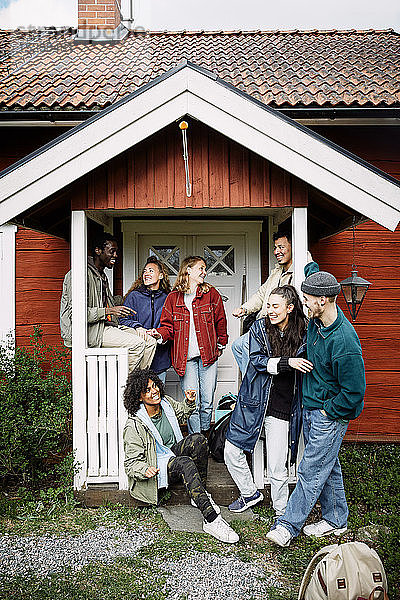 Glückliche männliche und weibliche Freunde unterhalten sich am Wochenende vor der Hütte