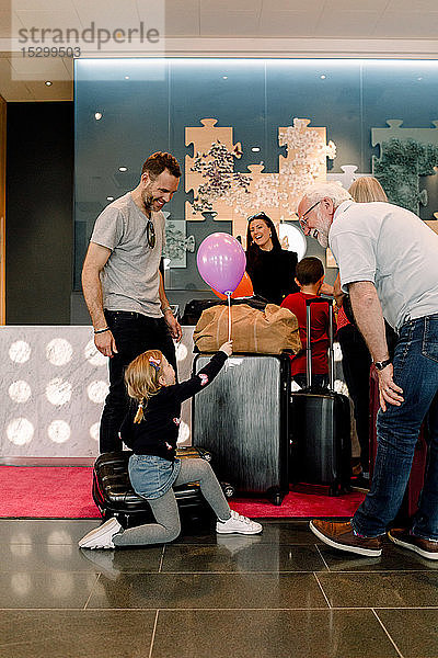 Eltern betrachten Mädchen mit Ballon in der Hand  während sie im Hotel auf einem Koffer sitzen