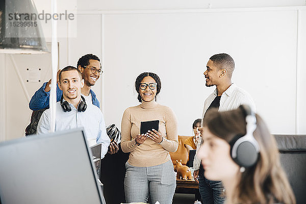 Lächelnde IT-Ingenieure reden  während sie im Kreativbüro an der Wand stehen