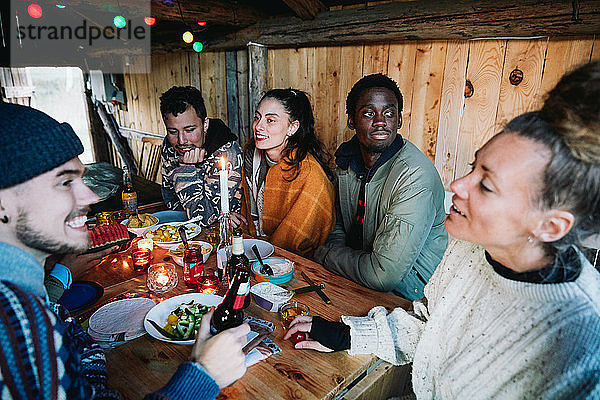 Männliche und weibliche Freunde unterhalten sich beim Essen auf dem Tisch im Blockhaus