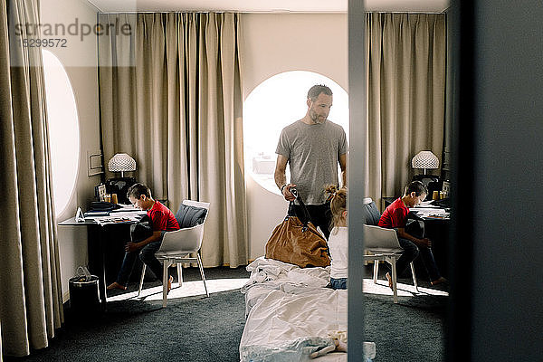Mann hält Tasche ans Bett  während Junge im Hotel am Tisch sitzt