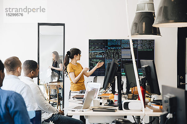 Weibliche Computerhackerin präsentiert Code auf dem Fernsehbildschirm während eines Treffens mit Programmierern im Kreativbüro