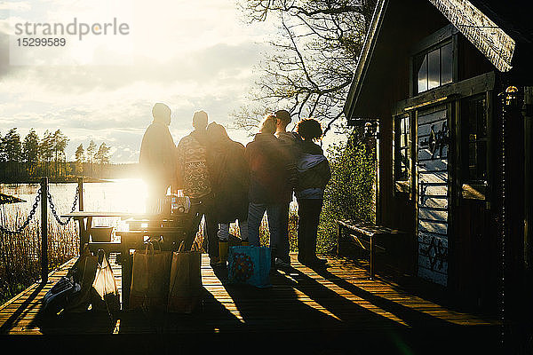 Scherenschnitt-Freunde schauen auf den See  während sie bei Sonnenuntergang vor dem Ferienhaus vor bewölktem Himmel stehen