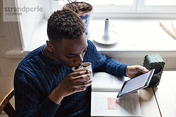 Hochwinkelaufnahme eines Teenagers  der schwarzen Kaffee trinkt  während er zu Hause mit einem digitalen Tablet E-Learning betreibt