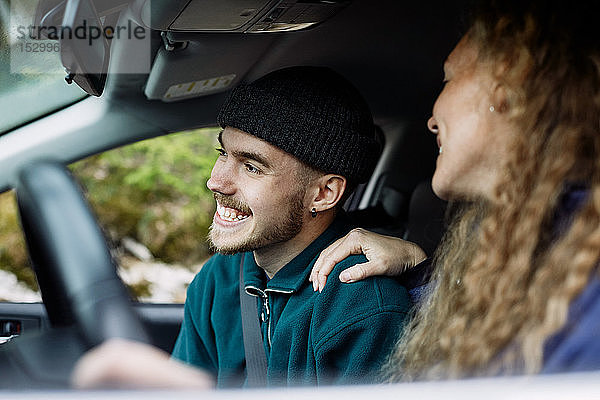 Junge Frau im Gespräch mit lächelndem männlichen Freund beim Autofahren