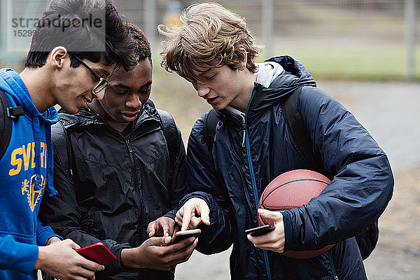 Freunde schauen in das Telefon des Teenagers  während sie mit dem Ball auf dem Spielfeld stehen
