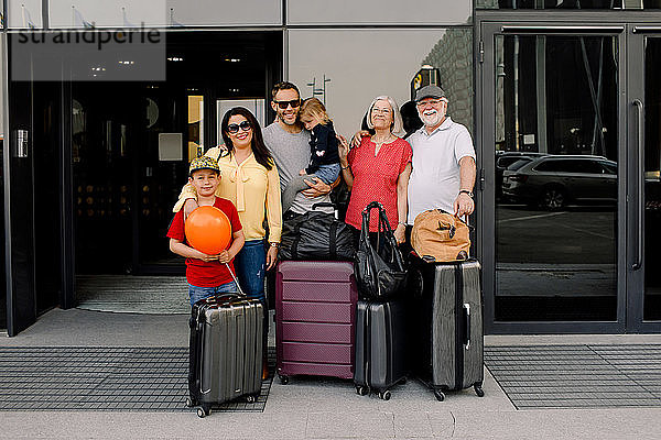 Porträt einer glücklichen Familie mit Gepäck steht am Hoteleingang