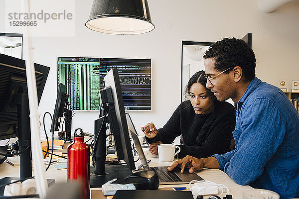 Fokussierte männliche und weibliche Ingenieure codieren über Laptop auf dem Schreibtisch im Büro
