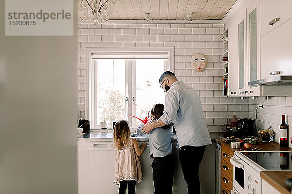 Mann steht mit Mädchen  während er der Tochter an der Küchenspüle assistiert