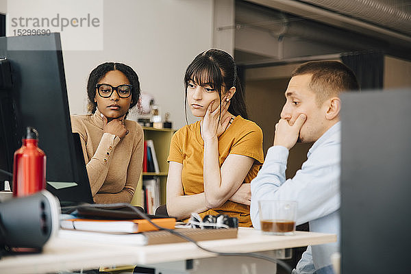 Fokussierte Computerprogrammierer schauen auf den Laptop  während sie gemeinsam am Schreibtisch im Kreativbüro arbeiten