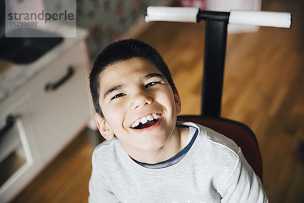 Hochwinkelansicht eines glücklichen behinderten Jungen  der zu Hause im Rollstuhl sitzt