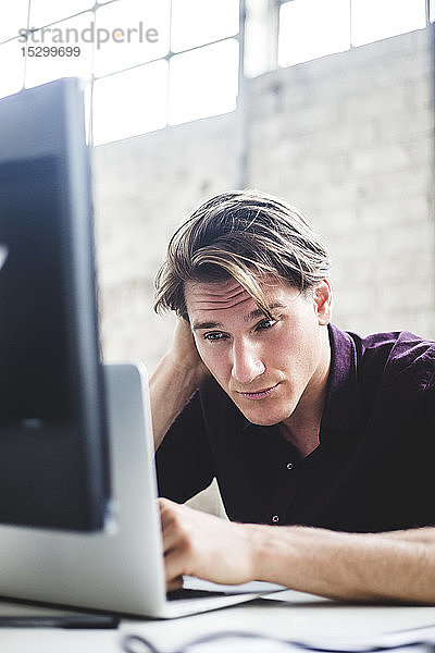 Junger männlicher Unternehmer arbeitet an einem Start-up-Projekt  während er am Schreibtisch im Büro kodiert
