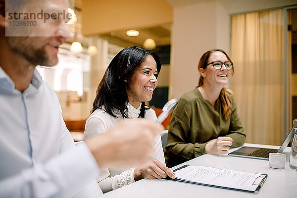 Lächelnde Geschäftskollegen arbeiten  während sie im Büro am Konferenztisch sitzen