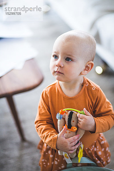 Hochwinkelansicht eines kleinen Mädchens  das weg schaut  während es Spielzeug im Wohnzimmer zu Hause hält