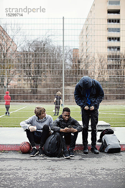 Telefonsüchtige Freunde auf dem Bürgersteig gegen Spielfeld in der Stadt