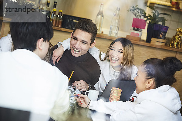 Freundinnen und Freunde lächeln  während sie in einem Café am Tisch sitzen