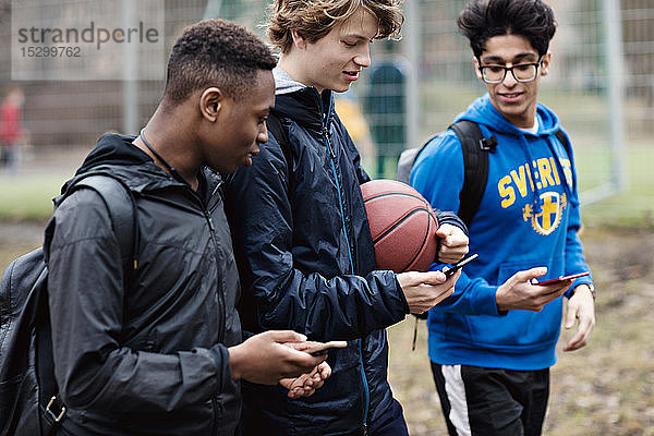 Freunde  die nach dem Basketballtraining auf der Straße mit Smartphones unterwegs sind