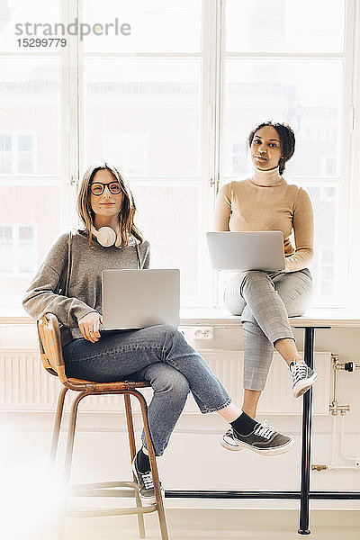 Porträt von Computerprogrammiererinnen mit Laptops  die im Büro am Schreibtisch sitzen