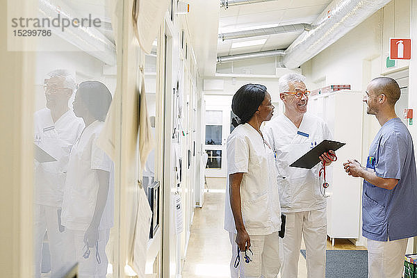 Lächelnde multiethnische Ärzte diskutieren stehend im Krankenhauskorridor